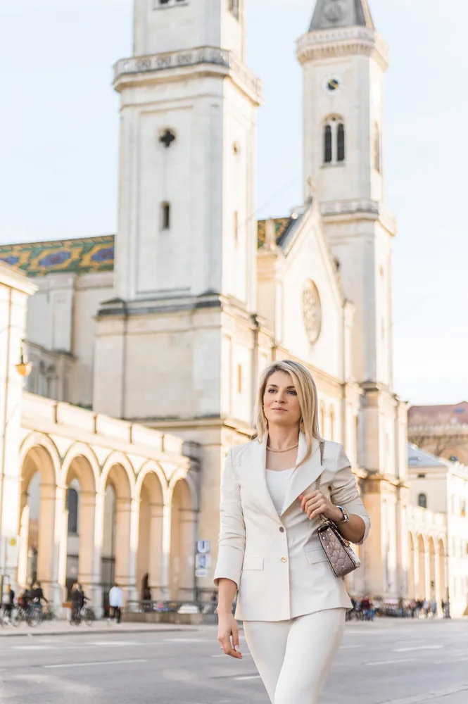 Woman in white suit walks past European-style church on sunny day.